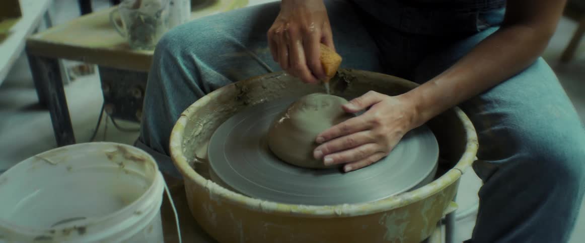A person in a denim apron is shaping clay on a pottery wheel
