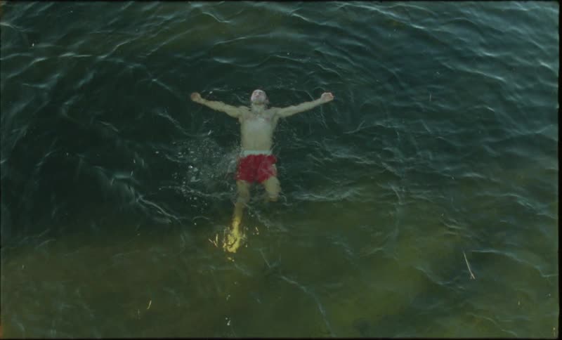 A man wearing red shorts floating on a lake in the morning