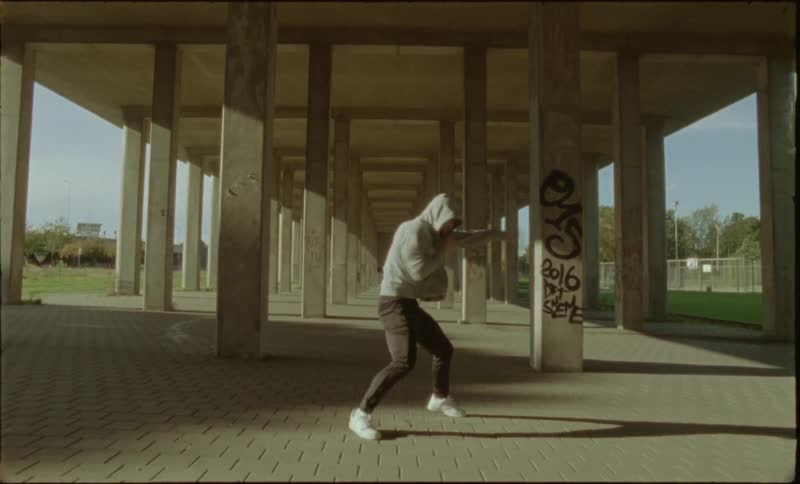Man in a hoodie training boxing drills under an overpass during the day