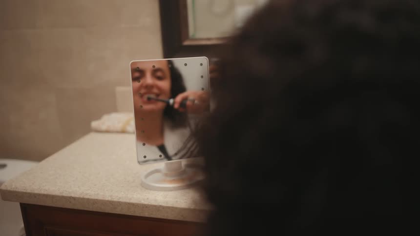 A handicapped woman brushing her teeth in the bathroom in front of a mirror
