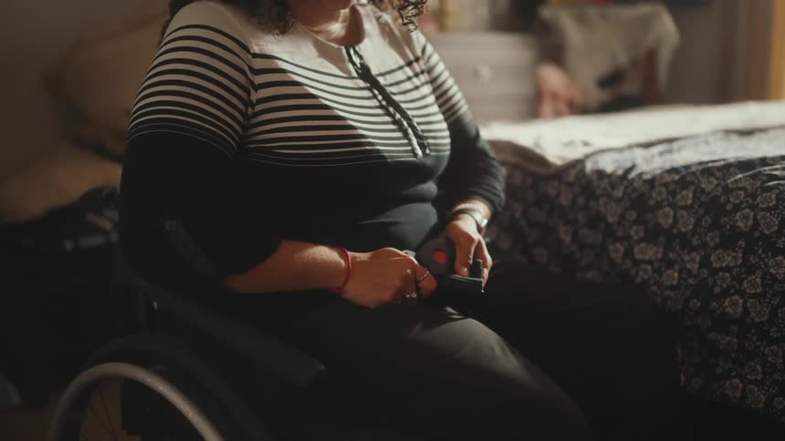 A woman fastens a seatbelt on a wheelchair in the bedroom