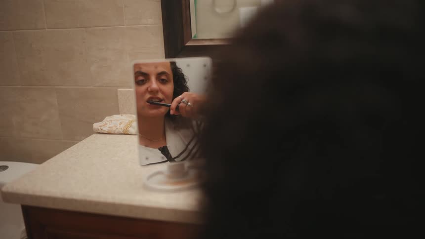 Disabled woman in a tabletop mirror brushing her teeth in the bathroom