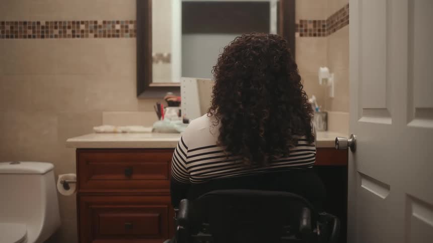 A woman in a wheelchair sitting in front of a bathroom sink
