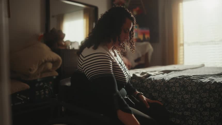 A young woman sits on a wheelchair to get out of the bedroom