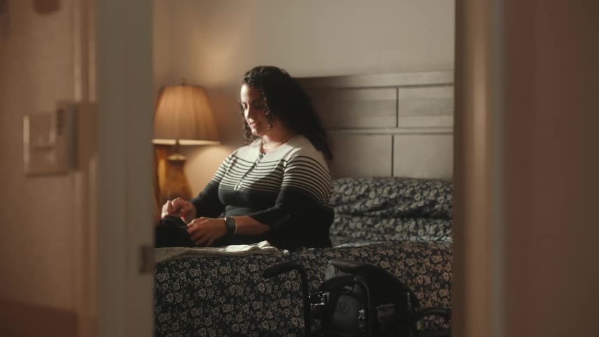 A woman helps a disabled woman get onto the bed in the bedroom