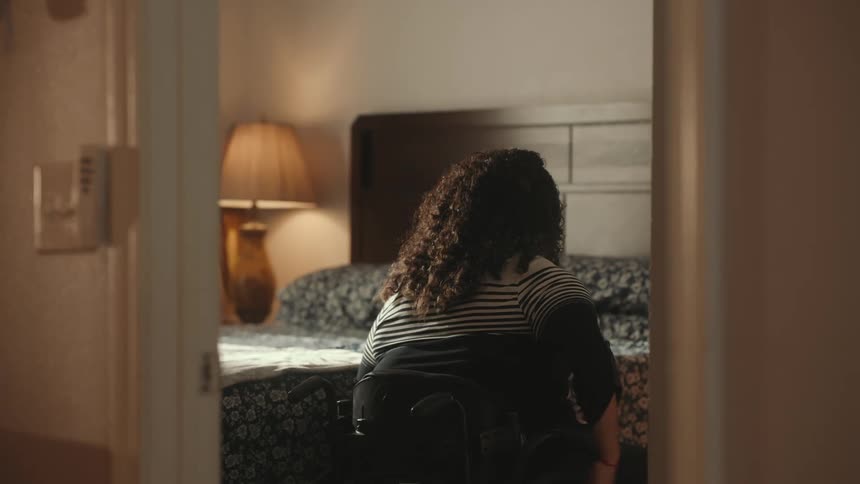 A mother helps her daughter to get off a wheelchair into bed