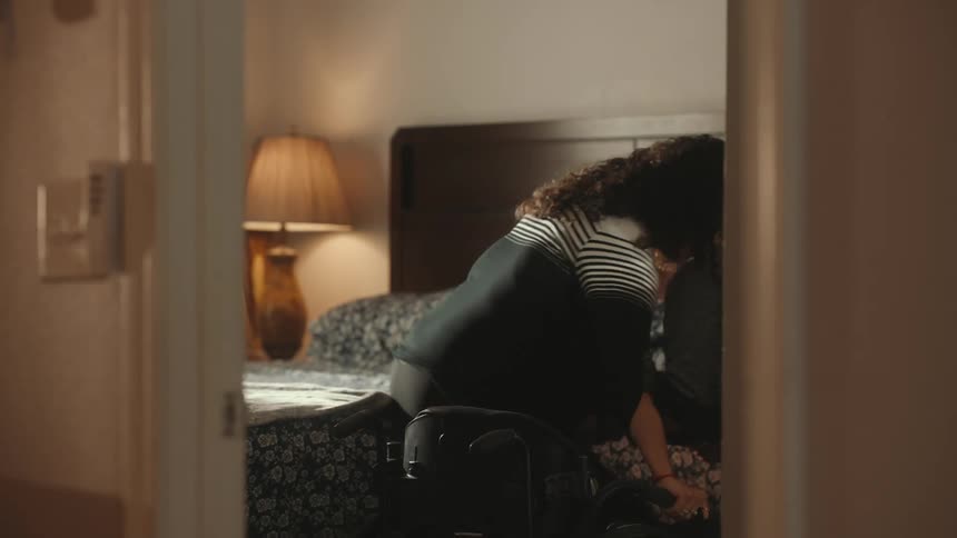 Female home aid helps woman from her wheelchair and onto the bed