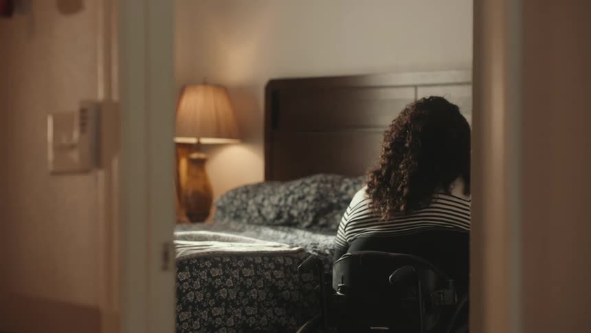 A woman gets out of a wheelchair to get on the bed