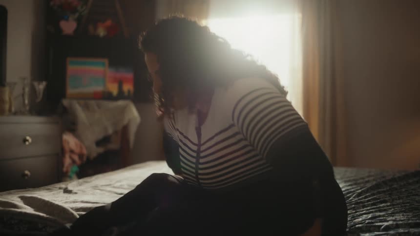 A paralysed woman sits up on her bed and pushes her legs out the side of the bed with her hands