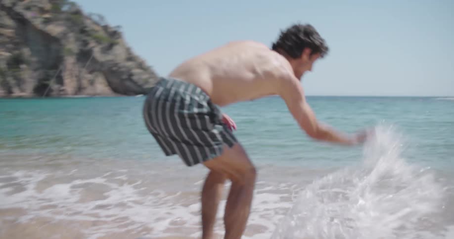 A man and a woman splash each other in the surf at a beach