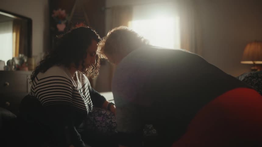 Mother helps daughter to get out of a wheelchair into a bed