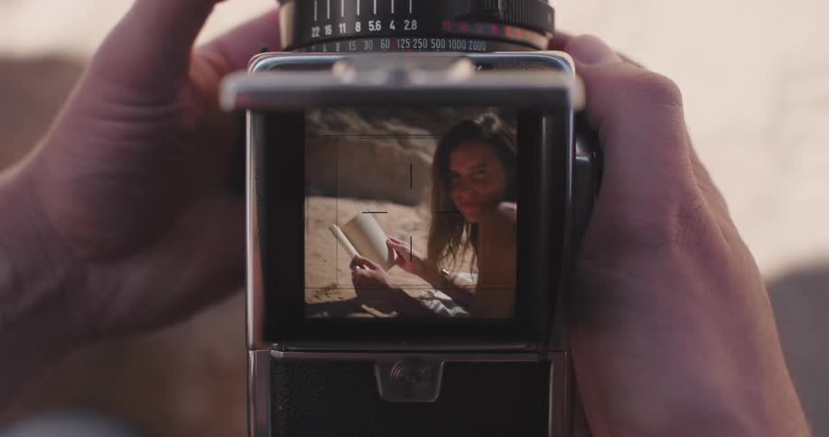 Vintage camera taking photo of a woman lying on the beach holding a book