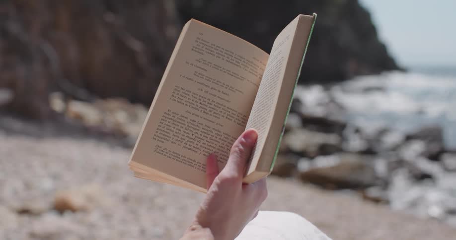 Closeup of a person holding a book with a beach in the background