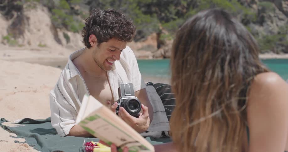 A man takes pictures of a woman reading a book in the beach
