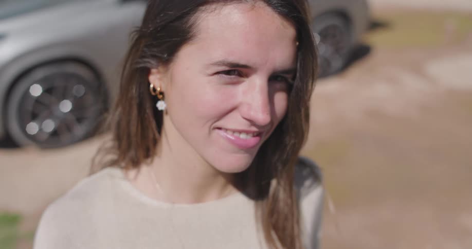 A clip of a lady smiling and standing beside a car