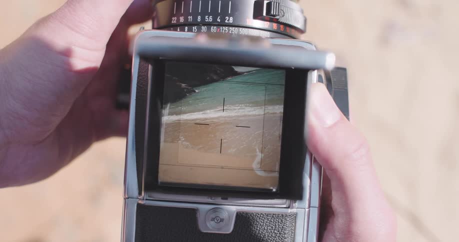 Womans hands holding a camera and looking at the viewfinder showing a beach
