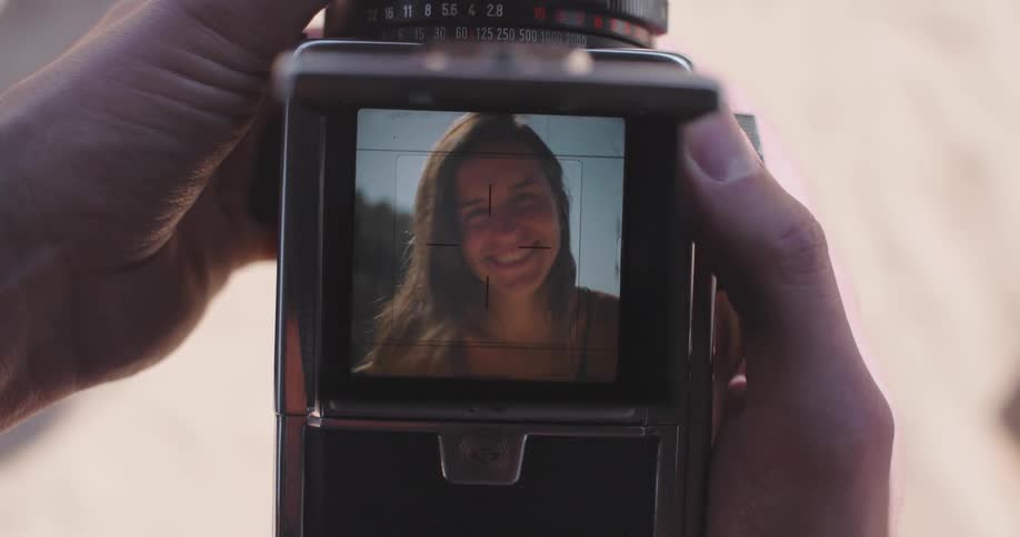 A man holding a camera with the viewfinder focused on a young woman