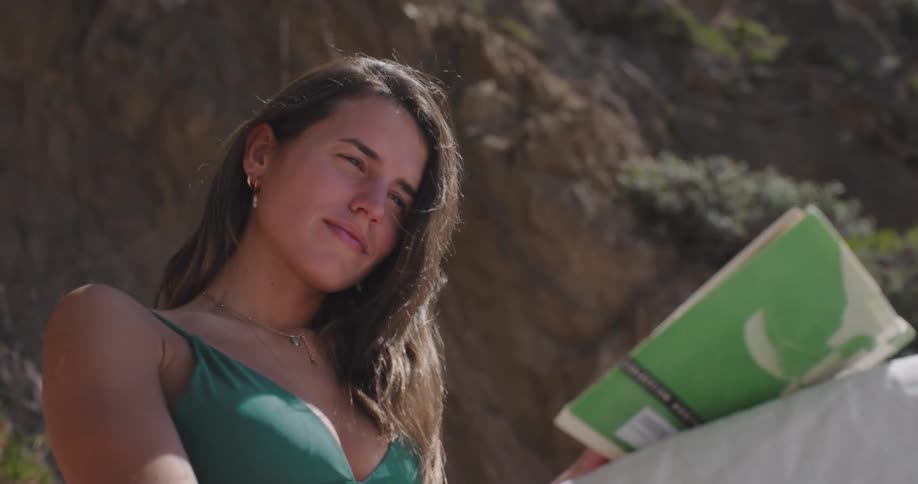 A young woman in swimwear reading a book outdoors