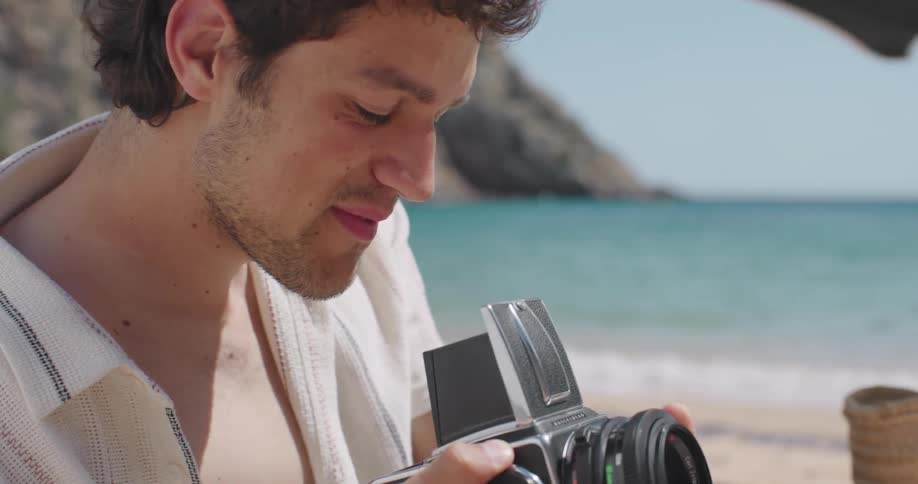 Man on a beach on a sunny day holding a camera and adjusting it to take pictures