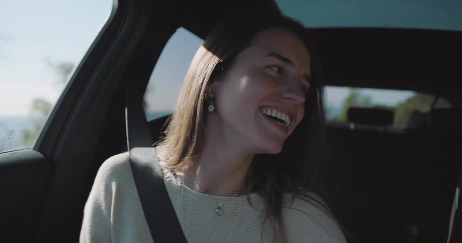 Woman sitting in the passenger seat of a car laughing and moving to the rhythm of the music