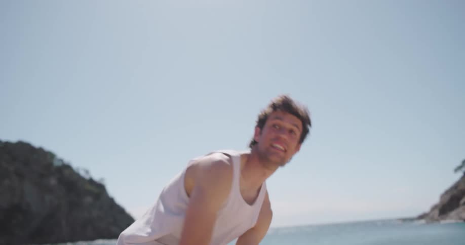Man running towards the sea on the beach taking off his sneakers pants and tshirt and calling his girlfriend along