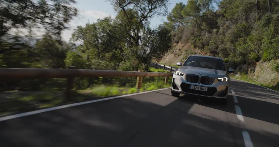 Front part of a bmw suv driving on an asphalt with mountains and greenery around