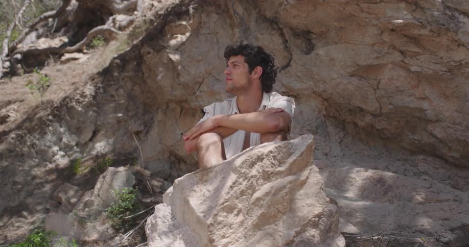 A young man sitting on a rock outcrop in the mountains
