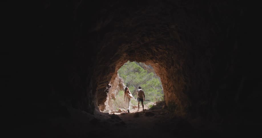 A man and a woman walk out of a dark cave