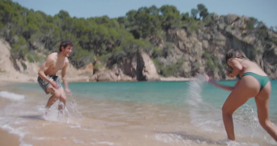 A young couple playfully splashing water in the coast of a tropical beach