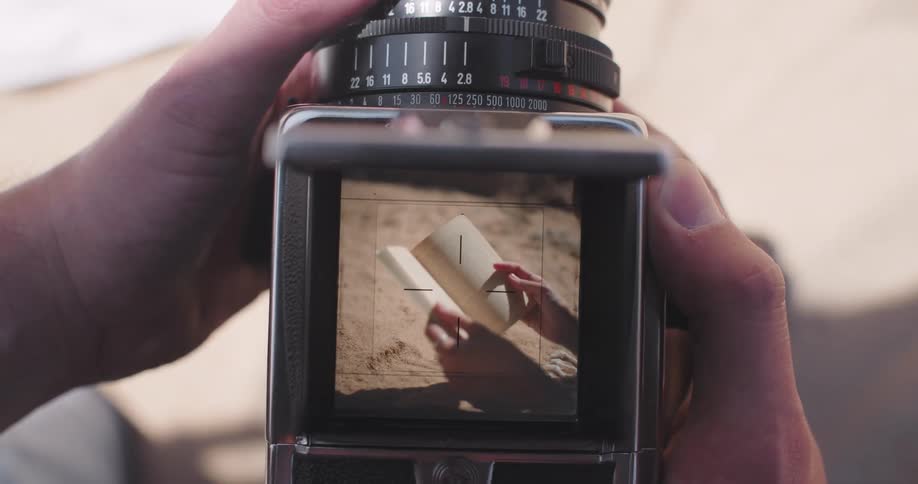 Closeup of a persons hand handling and taking photos of a woman reading a book on the beach sand