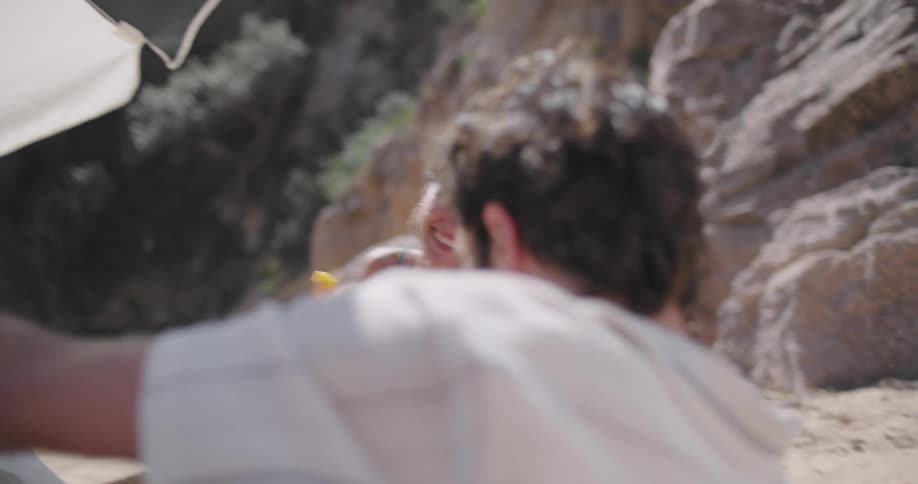 Woman putting a fruit in the mouth of her husband who was sleeping on the beach