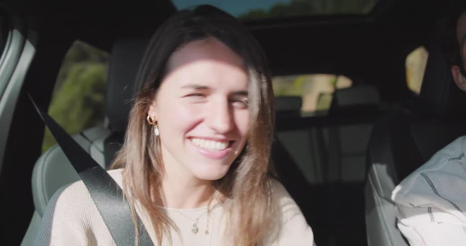 A young woman smiles and laughs while talking to her partner in a car