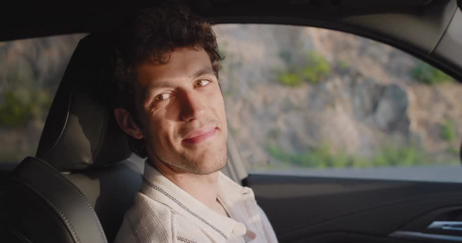 A man in the drivers seat of a car turns his head and smiles