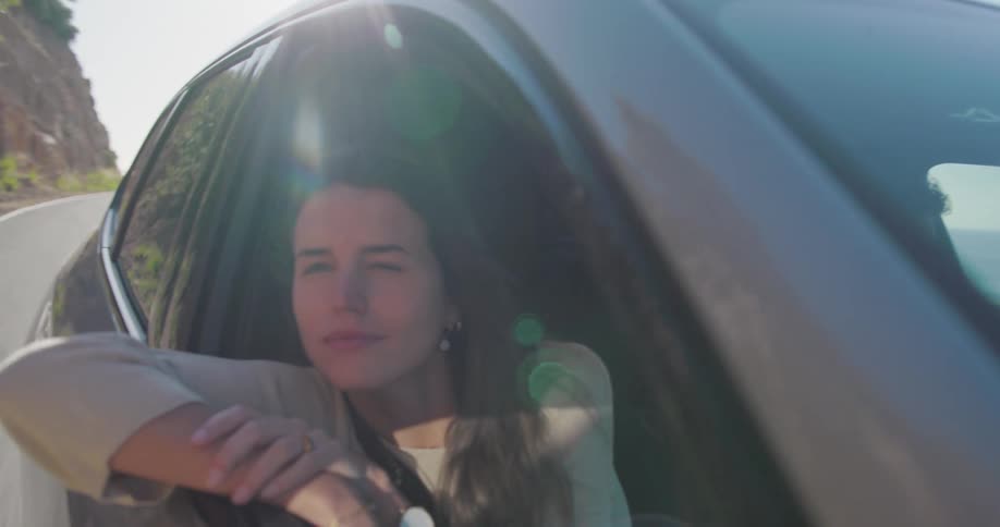 Female passenger leans out of car during a road trip on a coastal highway