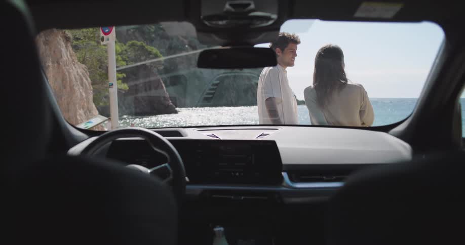 A young couple talking on the beach seen from the windshield of a parked vehicle