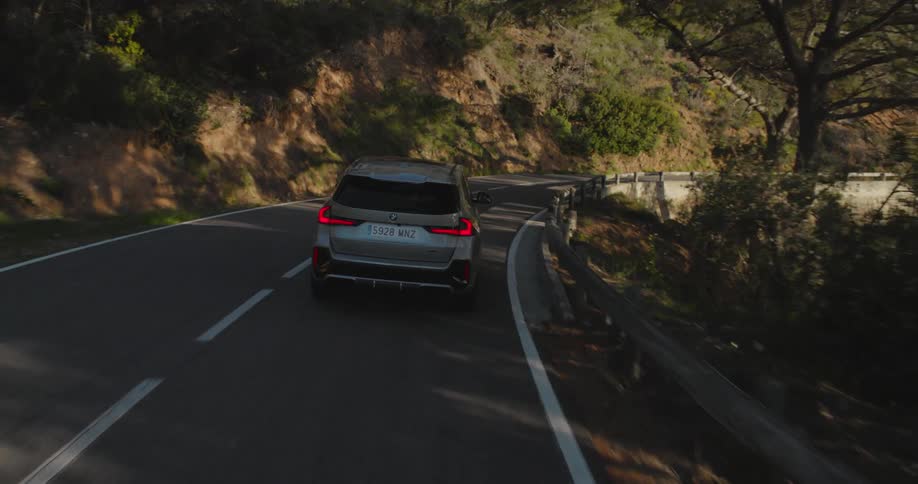 Rear view of a gray bmw traveling along the curves of a road with mountains and vegetation around it