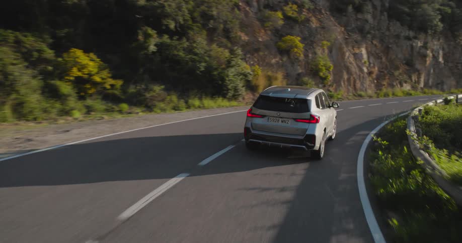 Bmw suv driving along a paved road with mountains and greenery around