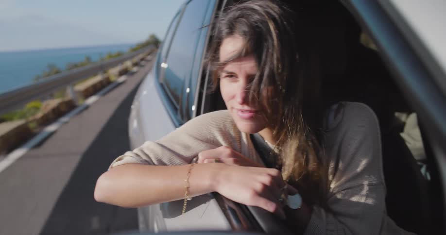 A woman sitting in the front seat of a car looks out of the window and enjoys the coastal view