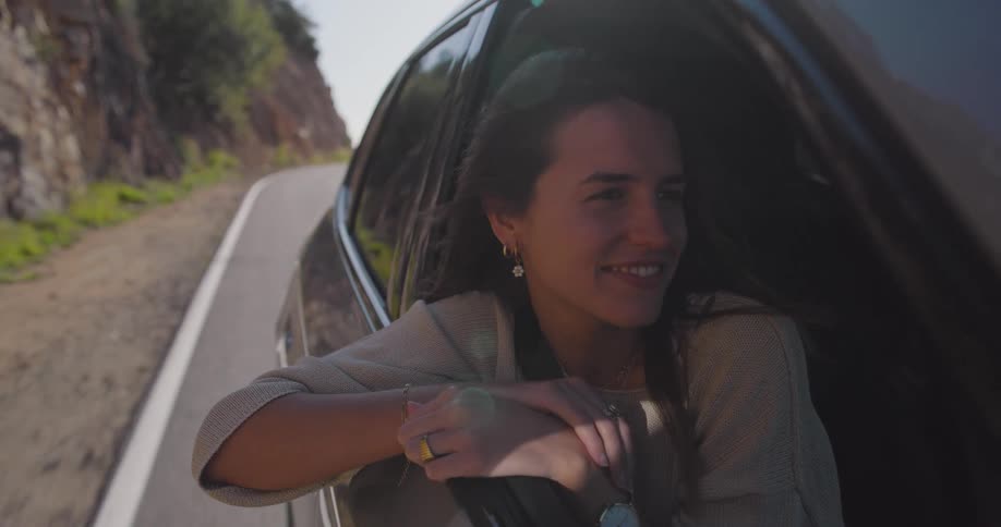 A young happy woman enjoys a road trip with her head out of the window