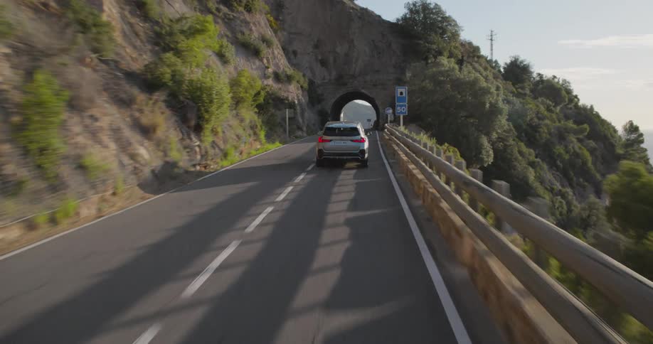 Vehicle drives along coastal highway passing through a tunnel near a large house
