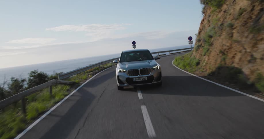 Bmw suv and traveling down a street with curves and vegetation around