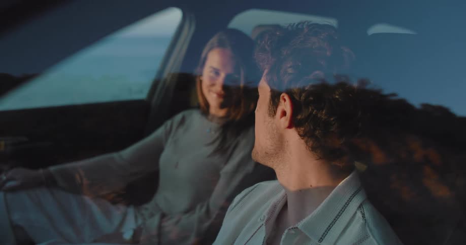 Couple exchanges glances while sitting in vehicle near the ocean