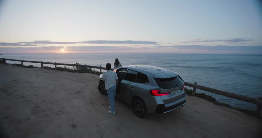 Man and woman getting out of the car and enjoying a view of the sunset on the horizon and the seafront