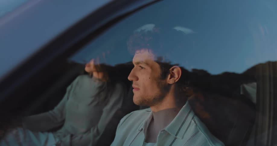 Young couple sitting on a car parked near the ocean looking at the sunset