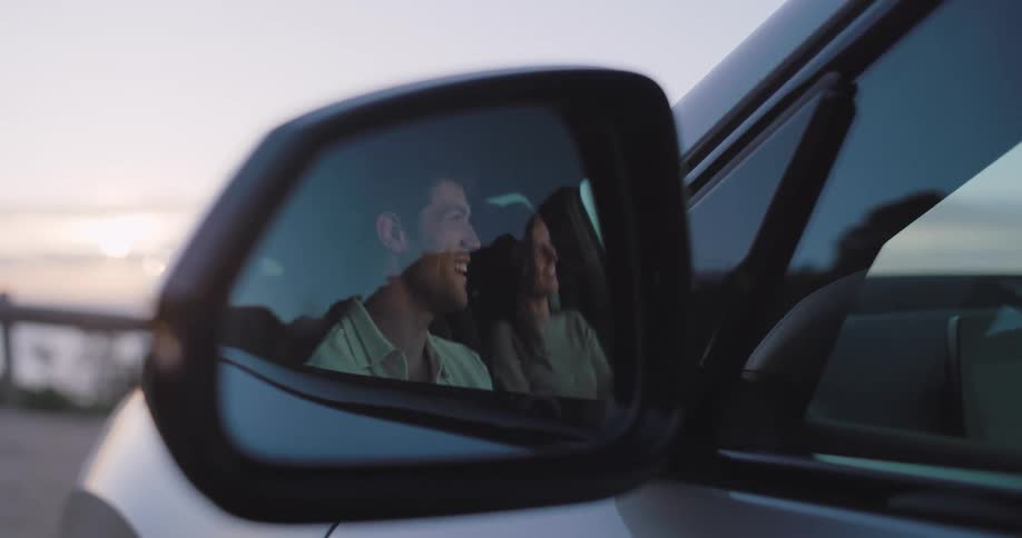 A young couple sitting in a car looking at the sunset