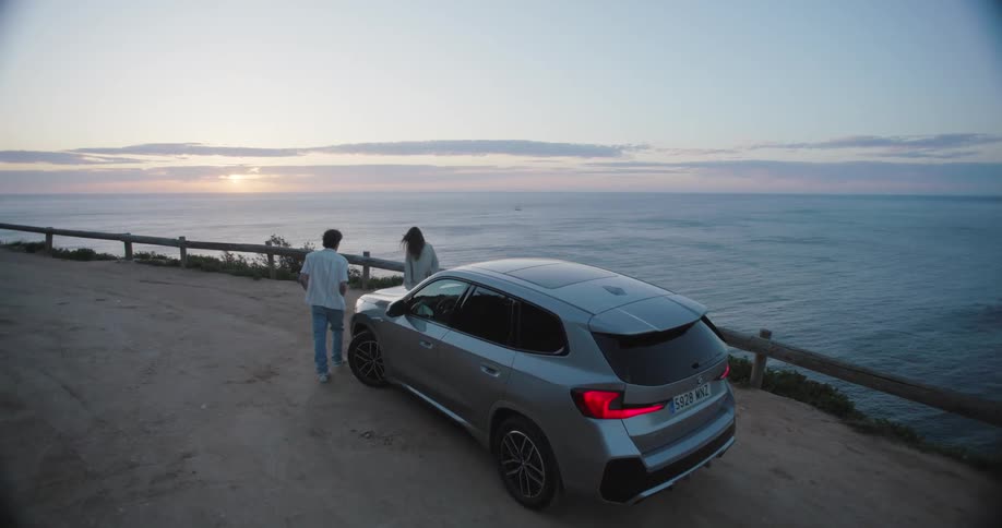 Man and woman getting out of a car to watch the sunset by a cliff overlooking the sea