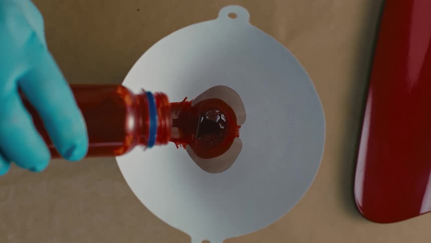 A person pours red paint from a small bottle