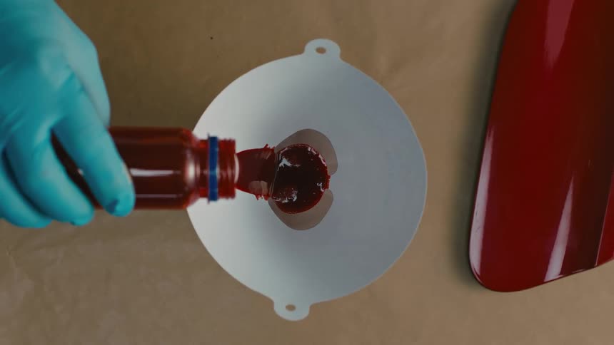 Hand with latex glove depositing red paint into a funnel