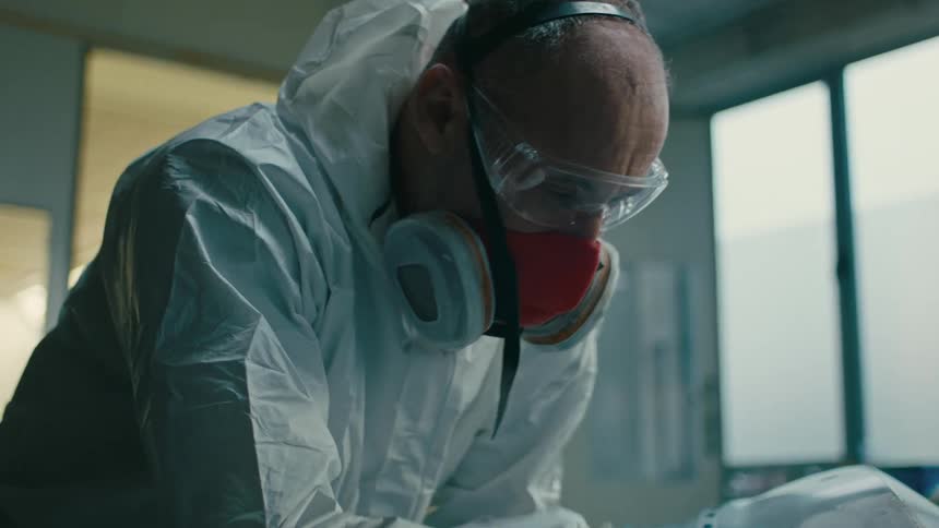 Individual in a white protective suit and blue gloves polishing a vehicle part