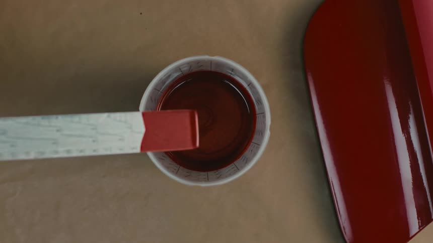 A person is mixing a small cup of red paint